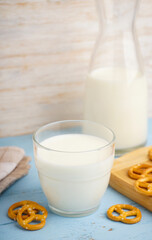 Glass and jug of fresh milk on wooden table against color background. Vertical.