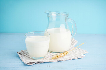 Carafe and glass of fresh milk on light blue background.