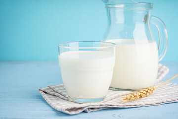 Jug and glass of fresh milk on wooden light blue background.