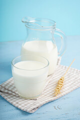 Carafe and glass of fresh milk on light blue wooden background.