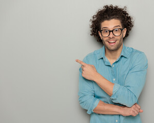 excited casual man with curly hair pointing finger to side and smiling