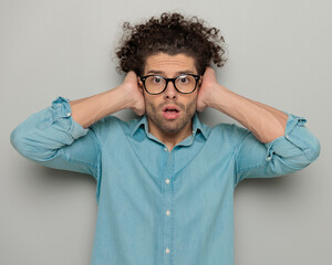 shocked young man with glasses covering ears, opening mouth and looking forward
