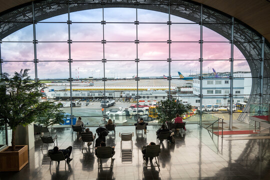 Paris, France - April 23, 2023: Tourists seated in the departure lounge looking out at the airfield through a large oval window at Charles de Gaulle Airport.