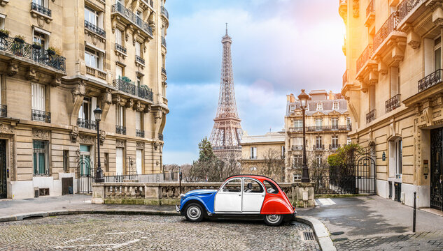 small paris street with view on the famous paris eifel tower on a cloudy rainy day with some sunshine - citroen 2CV in french national tricolour colors.