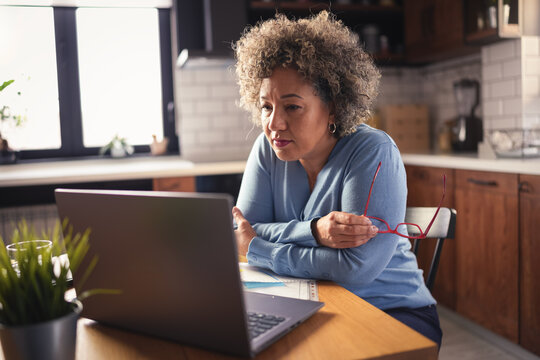 A Mature Entrepreneur Woman Of Mixed Race Working On A Computer At Home. Woman Small Business Owner. Woman Working On A Computer, Calculating Monthly Expenses, Mortgage Payments, Doing Home Budgeting