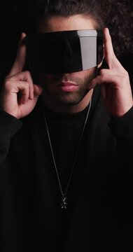 handsome cool man in black sweatshirt looking to side, rubbing palms and adjusting futuristic cyber sunglasses on black background