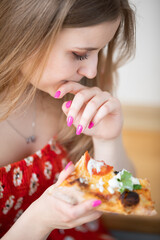 A girl dressed in a red floral shirt eats pizza.