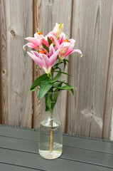 Bouquet of pink lilies in a bottle on a wooden background