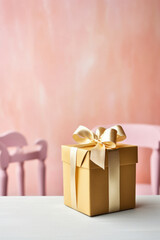 Gift box with golden bow on white table against pink wall background.