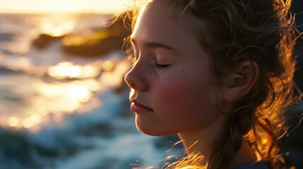 Scandinavian teenage girl meditates with her eyes closed, exposing her face to the sea breeze.