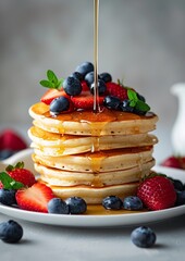 Pancakes with fresh strawberries, blueberry and maple syrup for a breakfast, honey pouring on delicious homemade pancakes with copy space. - obrazy, fototapety, plakaty