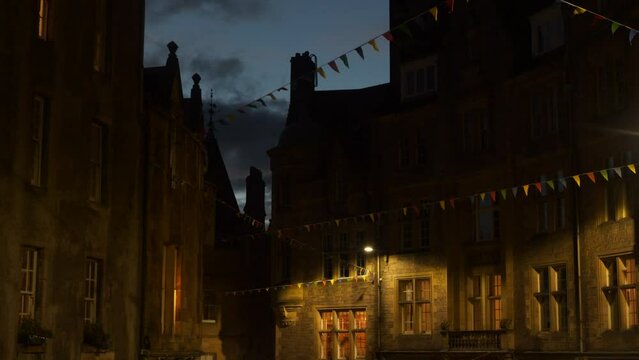 Colorful flags strung between charming town houses sway in the evening wind. Picturesque stone facades of historical buildings decorated with bunting flags. Festive mood in old part of historic city.