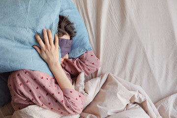 young woman in bed wakes up, insomnia, sleep disorder. person in sleep mask holds onto pillows,...