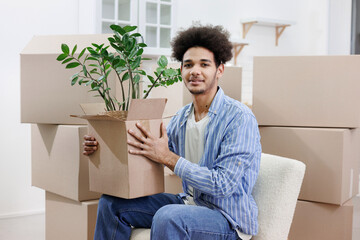happy young African American man moves into new home. person is sitting among cardboard boxes with...
