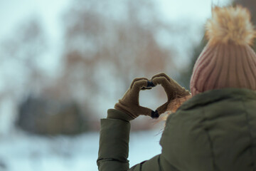 Modern woman outdoors in park in winter showing heart hands