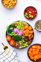 Vegan buddha bowl with pumpkin, quinoa, tomatoes, spinach, celery, edamame, tofu, cauliflower, broccoli and sesame seeds, white table background, top view. Healthy vegetarian comfort food