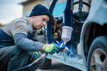 Fototapeta na wymiar Master car painter paints a car with a spray gun. Car painting at home.