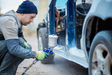 Master car painter paints a car with a spray gun. Car painting at home. - obrazy, fototapety, plakaty
