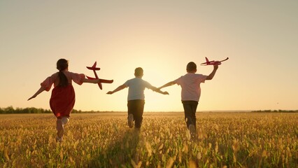 Happy children run with toy plane across field at sunset. Boy, girl wants to become pilot, an...
