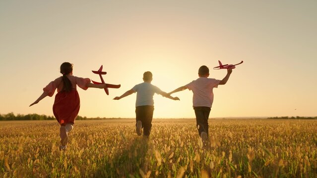 Happy children run with toy plane across field at sunset. Boy, girl wants to become pilot, an astronaut. Children play with toy plane. Slow motion. Teenager dreams of flying, becoming pilot. Childrens