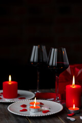 Saint Valentine's Day celebration. Red burning candles, hearts, gift box, postcard on dark wooden background. Happy holiday . Table decor for festive dinner, romantic atmosphere. Copy space for text