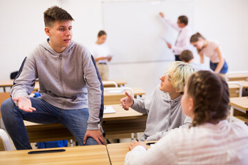 Portrait of teenager friendly talking with classmates during recess between lessons in classroom