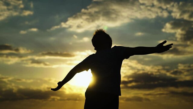 Boy Child raised his hands to sky in park at sunset, childhood dreams. Happy family. true faith. Little boy prays against background of sky, sun. Religion and god, Child boy plays in park against sky