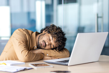 Businessman sleeping at workplace, young overtired and overworked man lying on desk inside office...