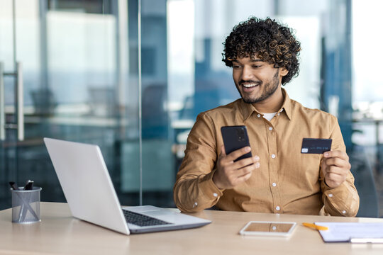 Businessman Inside Office With Telephone And Bank Credit Debit Card In Hands, Man Uses Application On Smartphone To Buy In Online Store, Satisfied Worker Inside Office With Laptop.