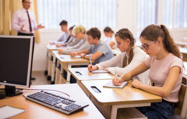 Fototapeta premium Multiracial group of teenage students working at class, listening explanations of teacher in classroom
