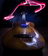 Music concept. Acoustic guitar isolated on a dark background under beam of light with smoke with copy space. Guitar Strings, close up. Selective focus. Fire effects. - obrazy, fototapety, plakaty