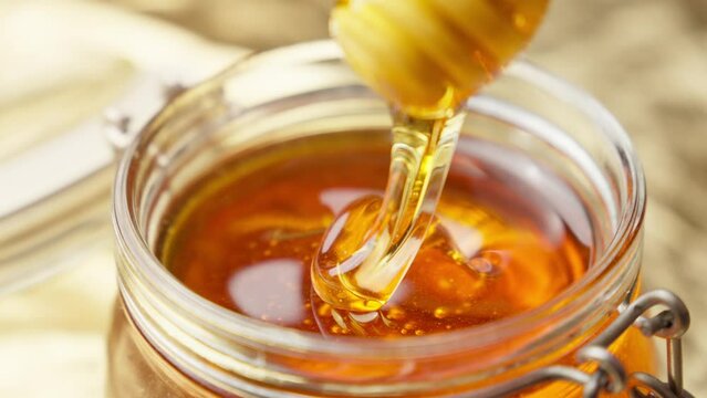 Honey dripping from wooden dipper. Healthy food concept. Honey in glass jar. Honey dripping from wooden honey spoon. Close-up in 4K, UHD