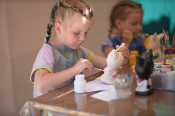 Naklejka premium Girls 4-5 years old are sitting at a table and painting with colorful paints. Children's creativity. Children's hobbies.