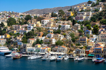 Fototapeta na wymiar Yachts at pier of Symi island. Greek mountainous island and municipality, part of Dodecanese island chain. Harbor town of Symi and adjacent upper town Ano Symi