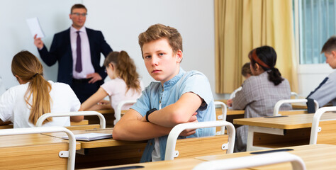 Fototapeta na wymiar Sad boy sitting at desk in a school class
