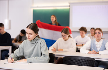 A young female student is carefully recording a lecture by a school teacher