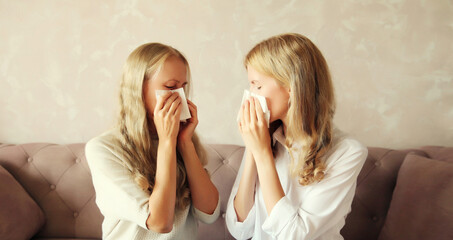 Sick exhausted middle-aged woman mother and adult daughter together sneezing blow nose using tissue at home - obrazy, fototapety, plakaty