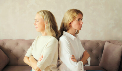 Upset offended caucasian middle aged mother or sister and adult daughter together sitting on couch...