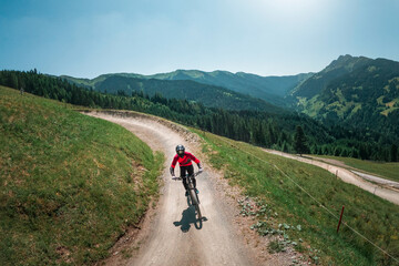 Downhill mountain biking in front of mountain scenery of Wilder Kaiser in the mountains of Austria, sunny blue sky day. - 704671953