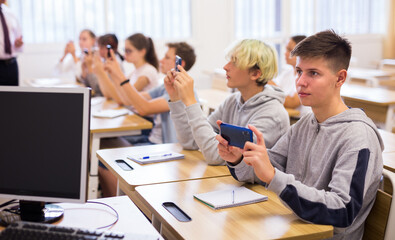 Teen students using smartphones to find necessary information on lecture in college class