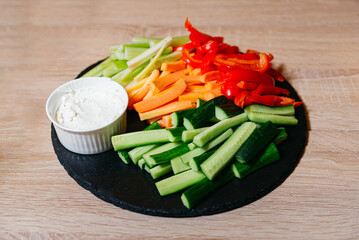 A black slate board adorned with vegetable sticks and a side of sour cream dip
