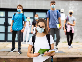 Girl in a protective mask with a backpack and notebooks going to college