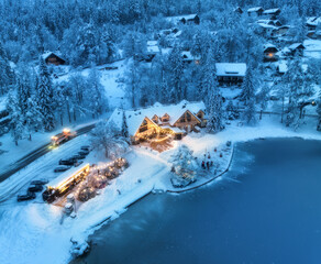 Aerial view of illuminated houses in fairy village in snow, forest, Jasna lake, street lights at...