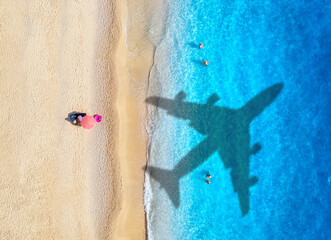Aerial view of blue sea, airplane shadow, sandy beach with umbrells at sunset in summer. Tropical...