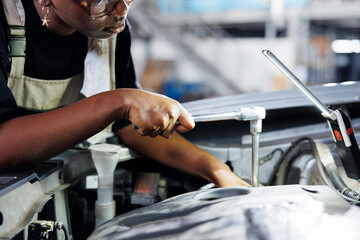 African american woman in car service using professional mechanical tool to repair broken battery....