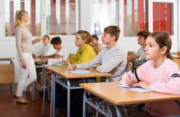 Fototapeta premium Portrait of cute intelligent schoolgirl who writing exercises at lesson in primary school