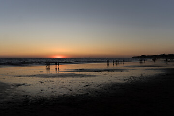 atardecer en la playa con siluetas negras de personas caminando por la orilla