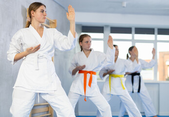 Team of teenage girls in kimonos uses new fighting techniques during karate lessons