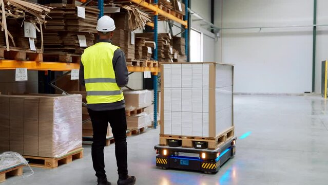 Warehouse worker manipulating with an industrial robot in modern industrial warehouse.