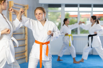 Concentrated adolescent girl in kimono honing punching techniques during kumite at karate training...